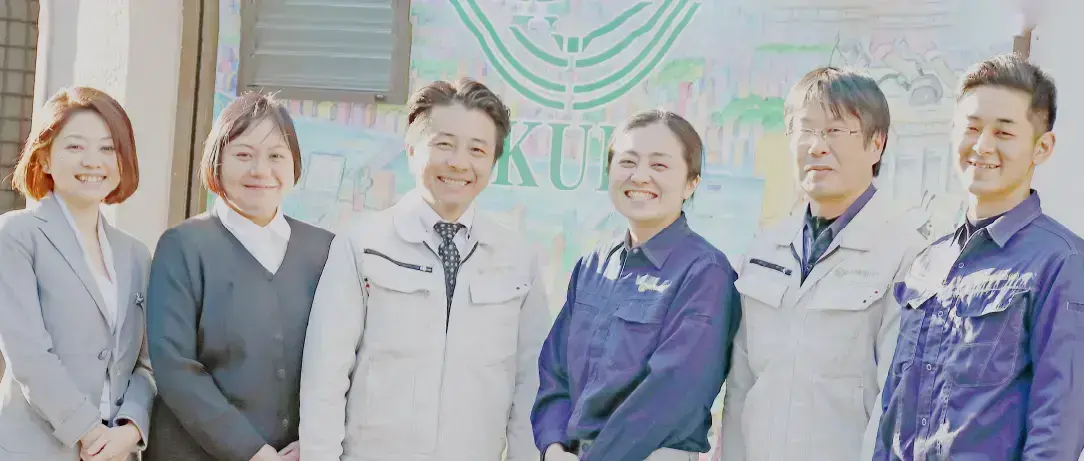 会社の前でスタッフたちが笑顔で集合写真に収まる様子。チームの一体感が伝わる。